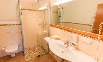 A modern bathroom with a shower and a sink. The walls are tiled in light colors and there is a large mirror.