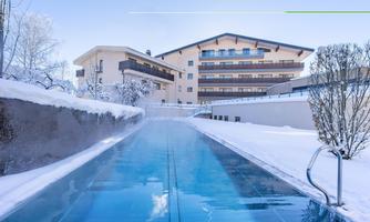 A modern hotel with an outdoor pool, surrounded by snowy meadows. The sky is clear and blue, creating a peaceful winter atmosphere.