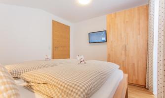 A cozy bedroom with two beds, a wooden dresser, and a television. The walls are light, and the ambiance is inviting.