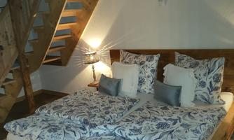 A cozy bedroom with a large wooden bed and pretty bedding. The warm wood tones and the staircase create an inviting atmosphere.