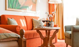 A cozy living room with an orange sofa and a small table. On the table are two wine glasses and a flower vase.