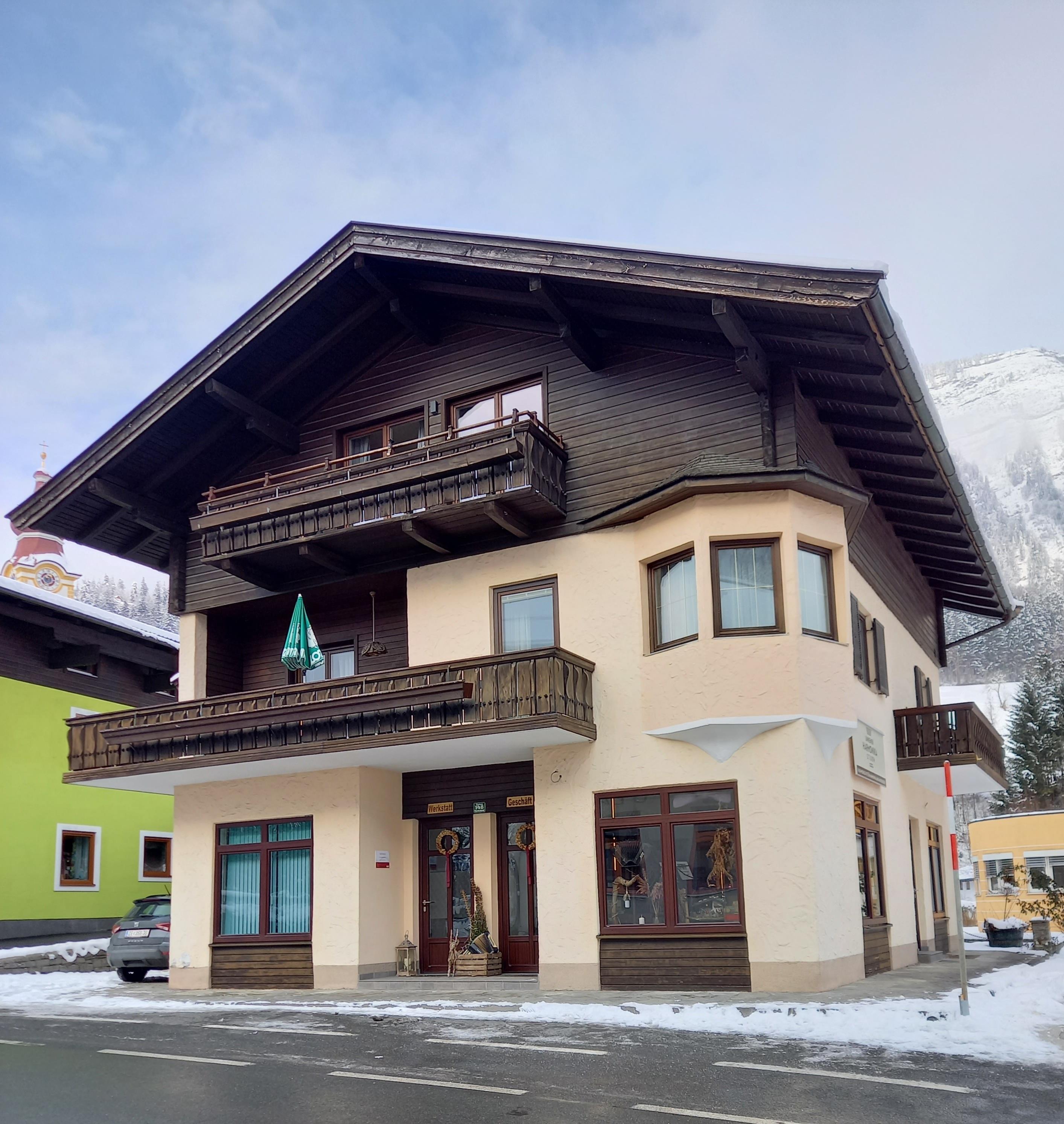 A traditional alpine house with a large balcony. It is situated in a snow-covered environment and has a clear sky in the background.
