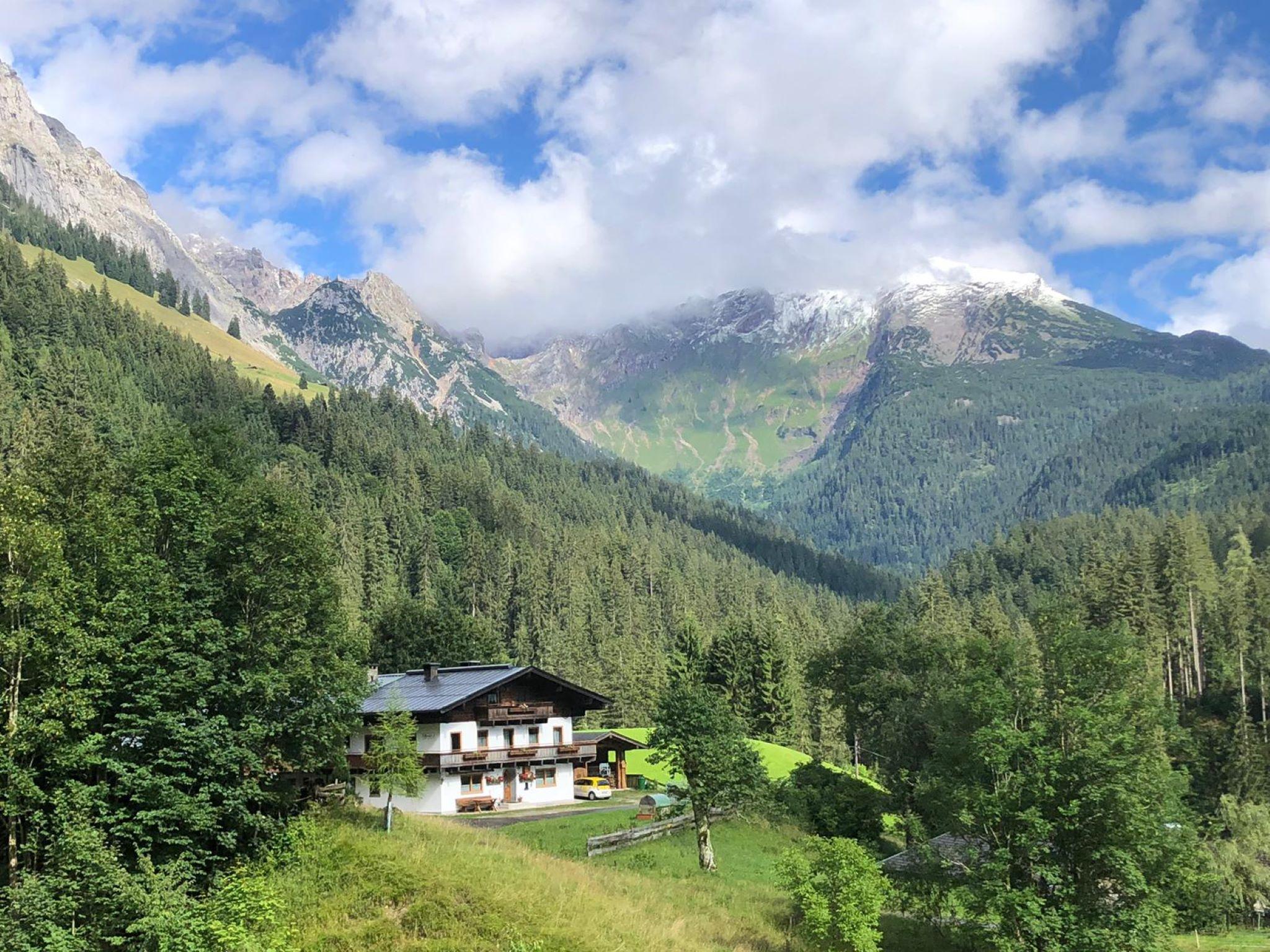 A picturesque landscape with a residential house in the foreground. In the background, majestic mountains rise under a partially cloudy sky.