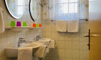 A bright bathroom with two mirrors and large sinks. The walls are tiled, and a window with a curtain provides natural light.