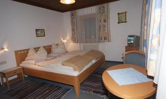 A cozy bedroom with a large double bed and two nightstands. A round table with a chair and a television are also present.