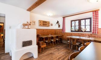 A cozy restaurant with wooden furniture and traditional decor. The ambiance is characterized by the windows with checked curtains and the warm wood paneling.