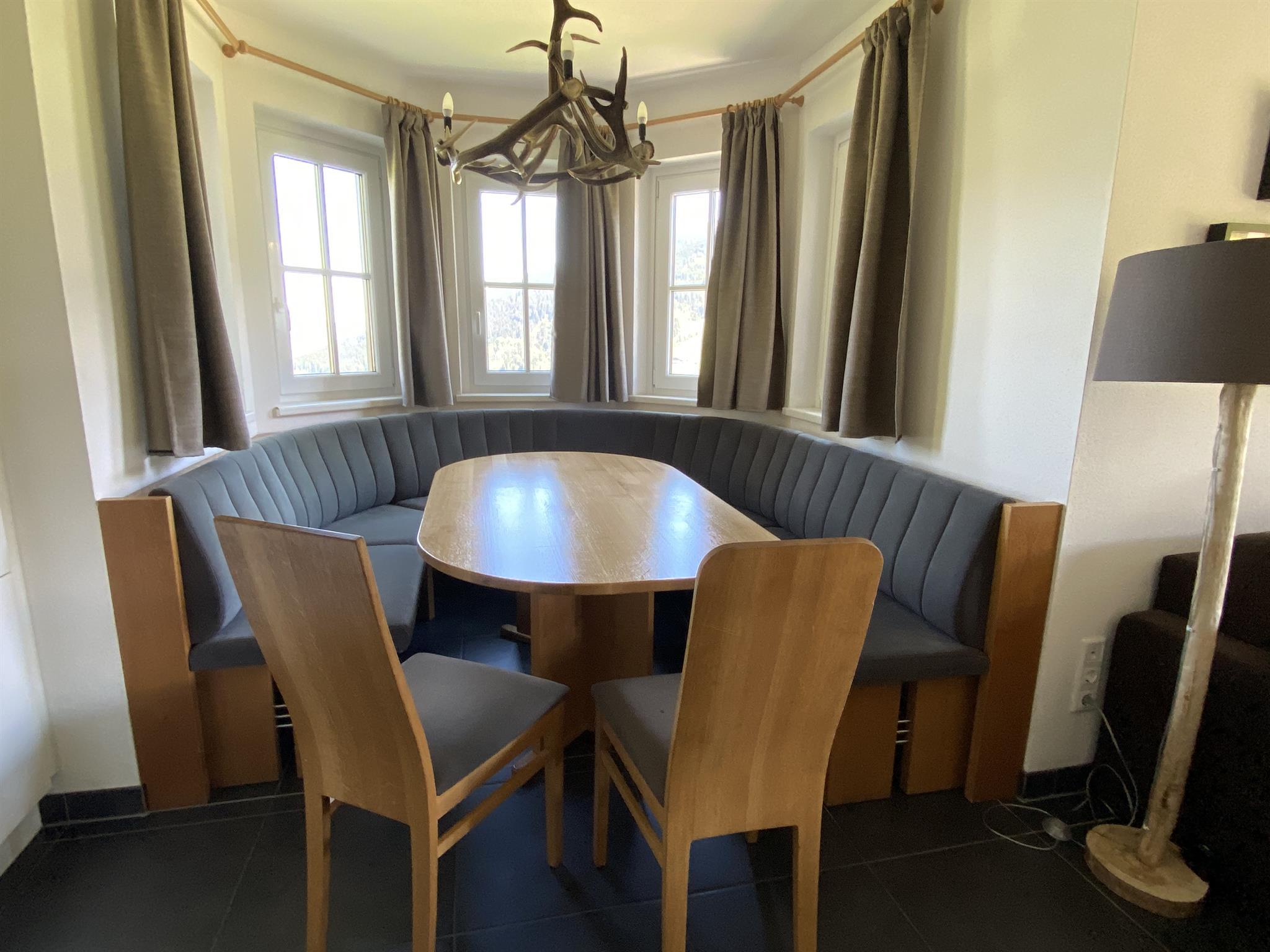 A cozy dining area with an upholstered bench and an oval table. Next to it are chairs and a modern lamp light.