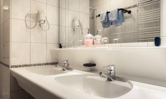 A modern bathroom with two sinks and a large mirror. Towels hang on a rod and hygiene products are placed on the sink.