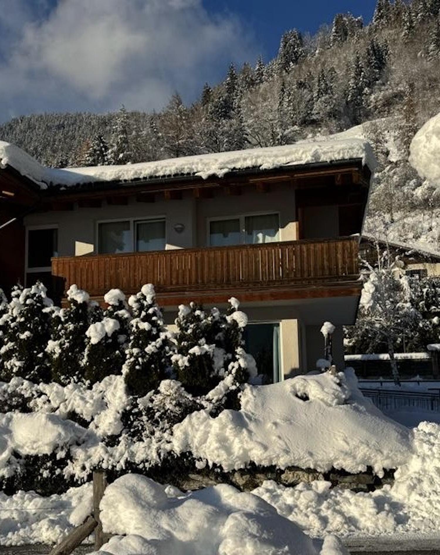 A cozy house with a balcony, surrounded by snow-covered trees. The snowy landscape radiates peace and winter scenes.
