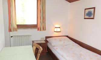 A simple bedroom with a single bed and a table. The room has a window with colorful curtains and a cozy lighting.