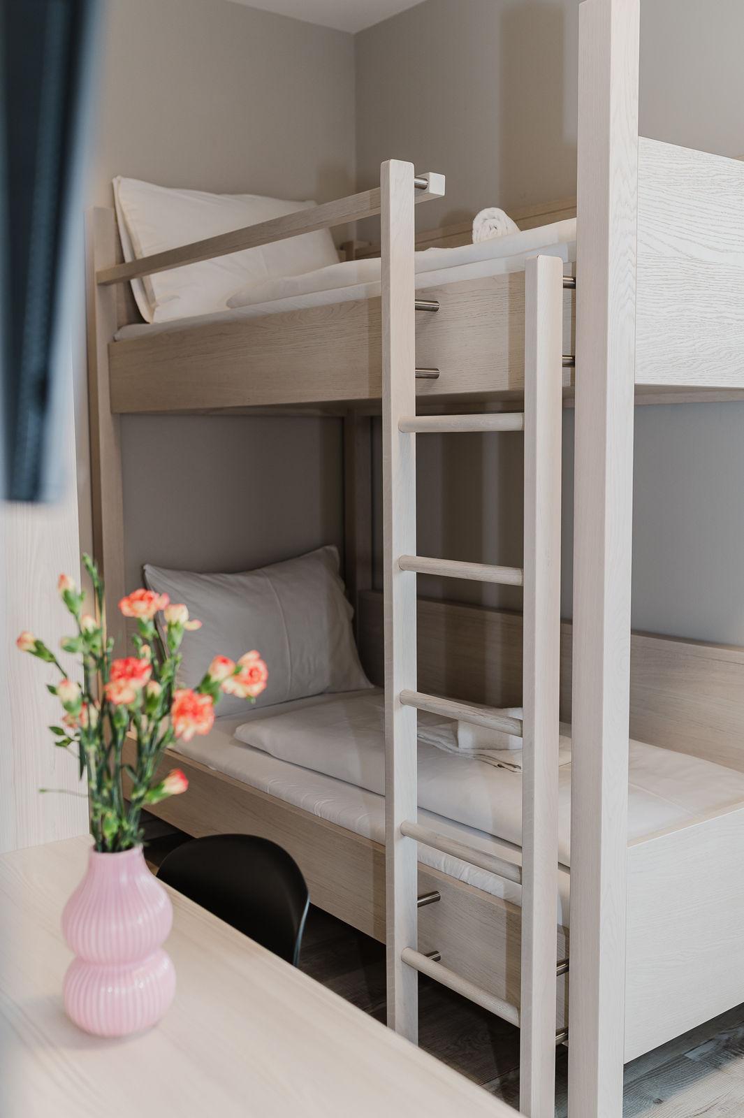 A modern loft bed in a neutral room. On the table stands a vase with colorful flowers.