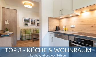 A modern kitchen with light cabinets and wooden shelves. The living area offers a cozy seating area with a comfortable sofa.