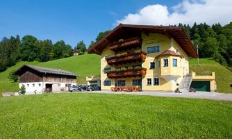 A charming farmhouse with beautiful balconies and a well-maintained garden. In the background, green hills and trees are visible.