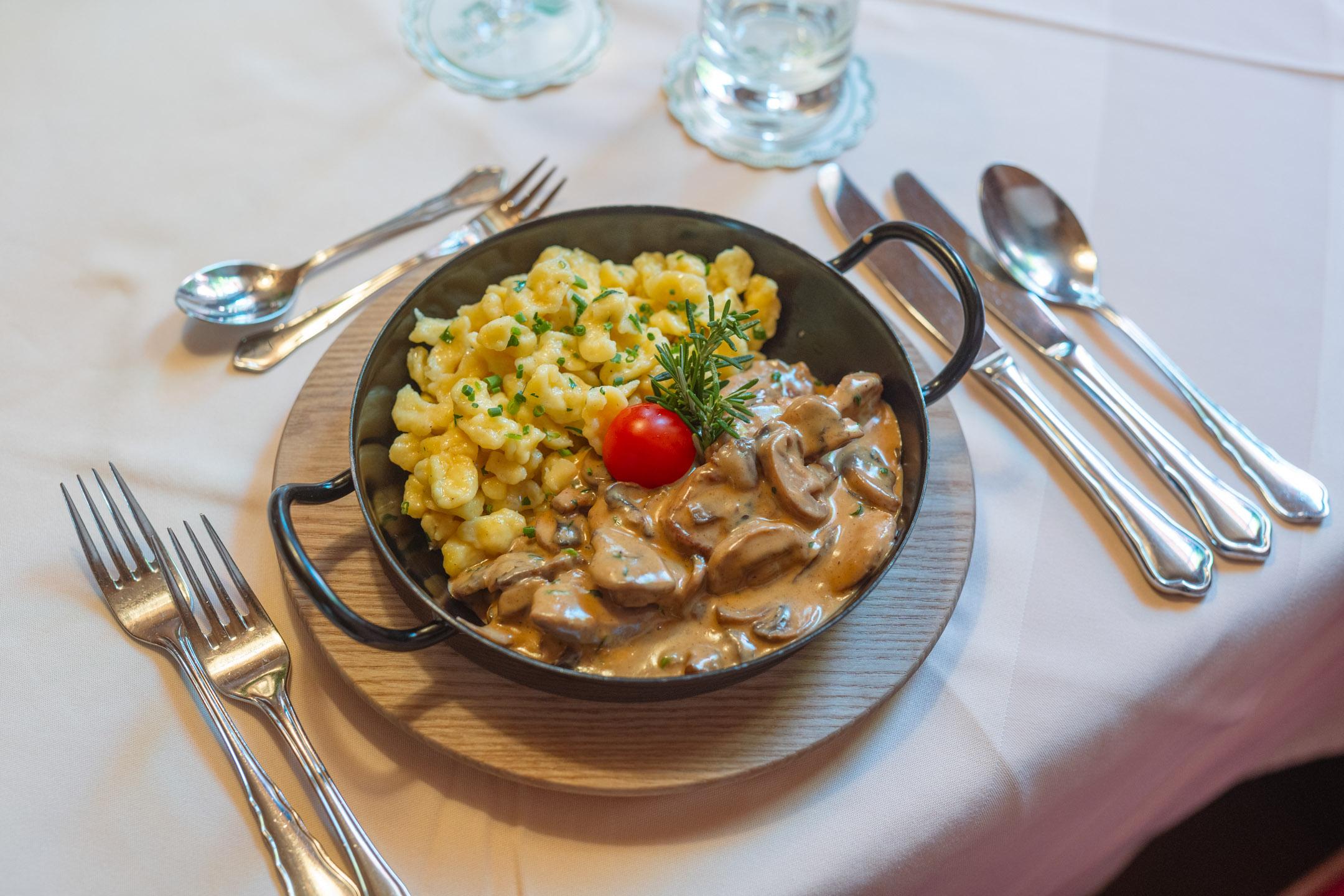 A deliciously arranged plate with meat in a creamy sauce and spaetzle. Topped with a tomato and fresh herbs.