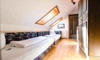 A bright room in the attic with two beds and large windows. The floor is wooden and there is a wardrobe on the wall.