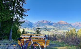 A beautiful view of the mountains with a bench in the foreground. A mountain bike is standing on the grass beside it.