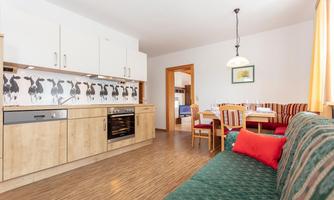 A modern kitchen with wooden cabinets and a cozy seating area. The dining area is inviting and bright with a large table and comfortable chairs.