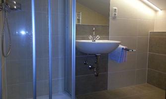 A modern bathroom with a shower and a sink. The walls are tiled in light colors, and there is a red carpet on the floor.