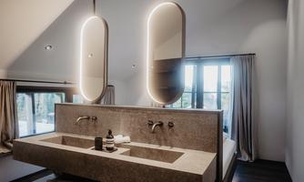 A modern bathroom with an elegant double sink and stylish mirrors. Large windows let in plenty of light and offer a view outside.