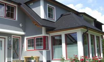 A modern house with a gray facade and red window frames. The garden is designed with colorful flowers and a small seating area.
