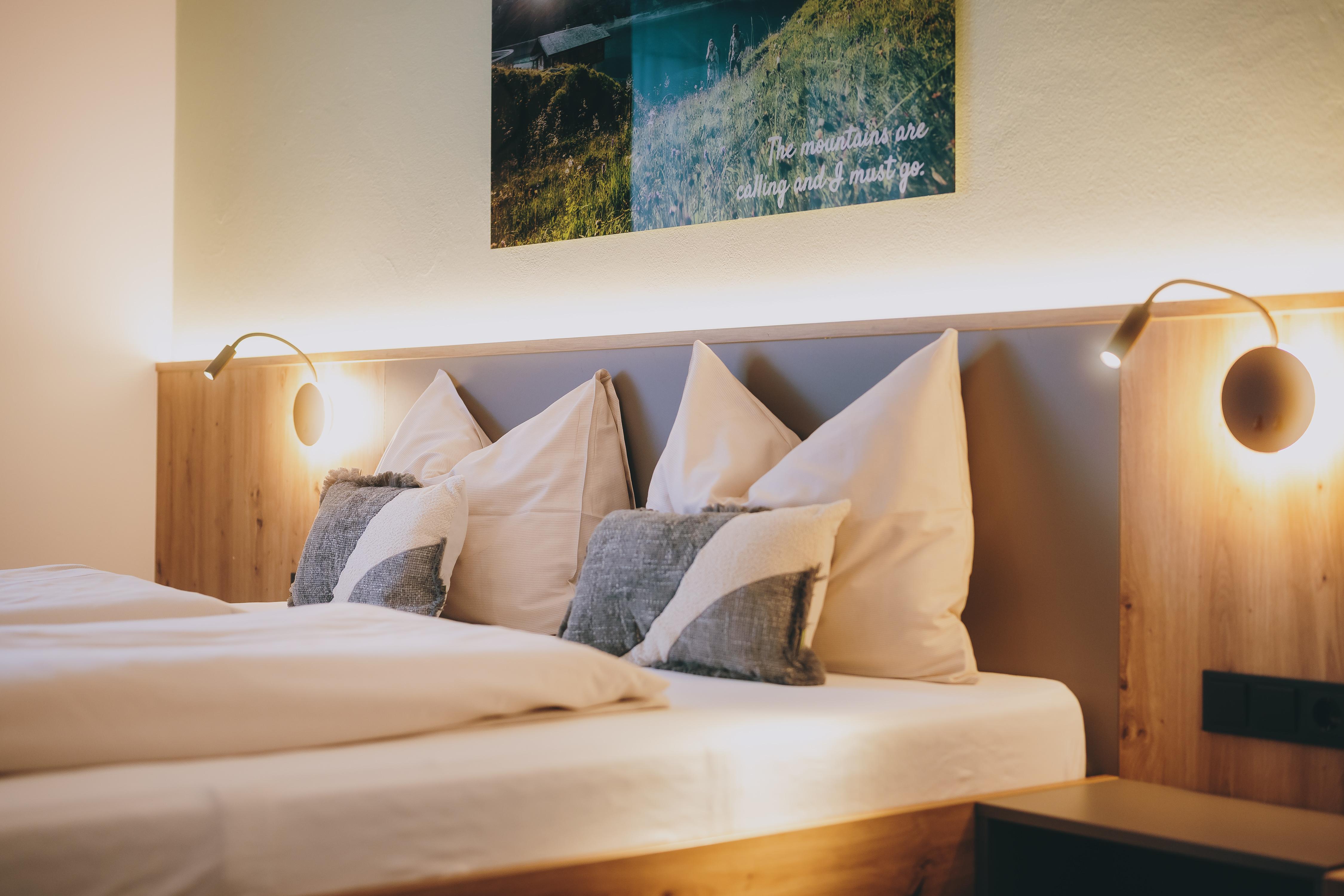 A modern bedroom with two beds and cozy pillows. Soft lighting and a decorative picture on the wall create a relaxed atmosphere.