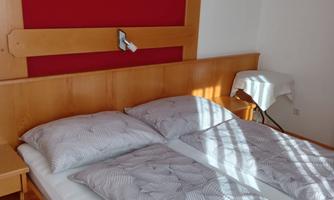 A cozy bedroom with a double bed and modern comforters. On the wall, there is a red accent with a mountain motif.