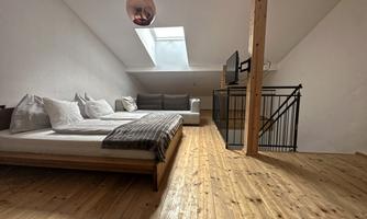 A cozy bedroom with a large bed and a bright wooden ceiling. A sofa and a television complement the modern decor.