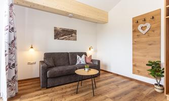 A cozy living area with a gray sofa and a small table. The walls are light, and there are decorative elements like a picture and a wall decoration.