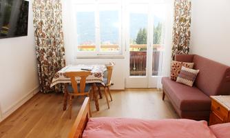 A cozy room with a sofa, a dining table, and a beautiful view through large windows. The decor is bright and inviting.