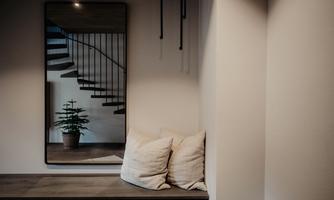 A modern entrance area with a mirror and a cozy seating area. In the background, a stylish staircase is visible.