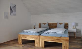 A bright room with two wooden beds and blue bed linen. Pictures hang on the wall and there are nightstands with lamps.