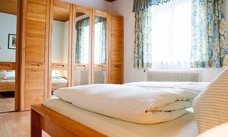 A cozy bedroom with a large bed and wooden-clad wardrobes. The windows are adorned with colorful curtains and let in plenty of daylight.