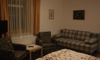 A simple living room or bedroom with two beds. There is a sofa, two chairs, and a small table.