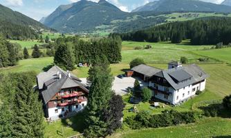 A picturesque landscape with two traditional houses and lush greenery. In the background, gentle mountains and a clear sky can be seen.