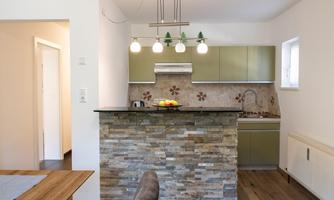 A modern kitchen with green cabinets and a stone bar. Bright lighting and wooden flooring create an inviting atmosphere.
