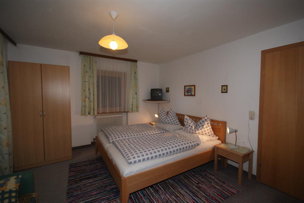 A simple bedroom with two beds and checkered bedspreads. The room is bright and has a wooden wardrobe as well as a small television.
