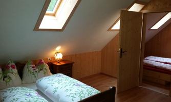 A cozy bedroom with two beds and colorful pillows. A wooden desk and a door leading to another room.