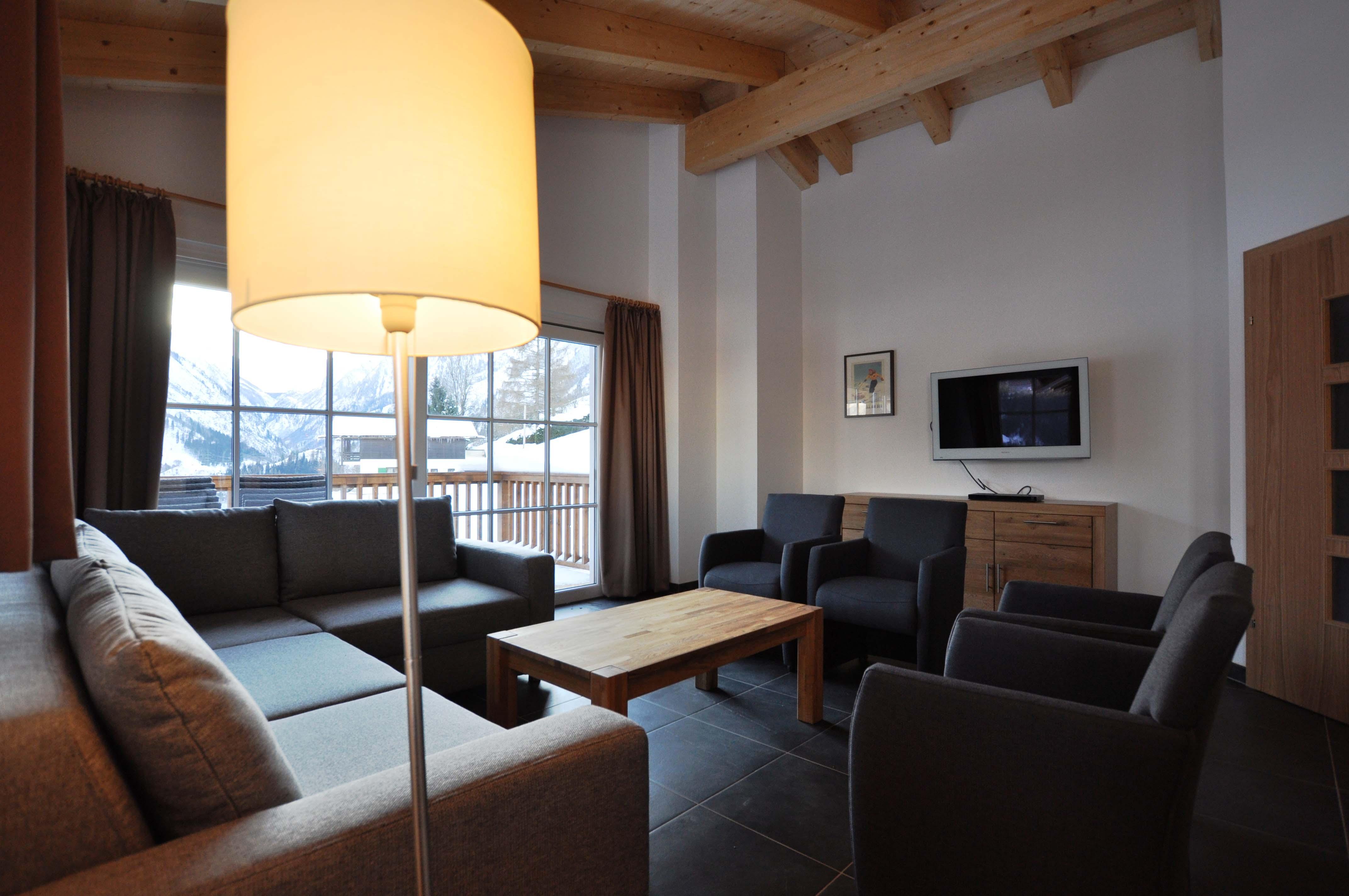 A modern living room with a cozy sofa and chairs. Large windows let in plenty of daylight and offer a view outside.