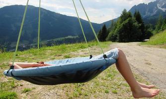 A hanging lounger in nature with a view of mountains and trees. Someone is lying relaxed on the lounger and enjoying the view.