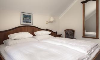 A cozy bedroom with a large double bed and a wooden frame. A picture hangs on the wall, and a mirror stands next to it.