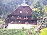 A traditional wooden house in the midst of beautiful nature. It has balconies with colorful flowers and is surrounded by trees.
