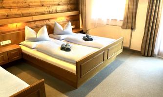 A cozy hotel room with two beds and wood paneling. The rooms are bright and cheerful, with windows and upholstered beds.