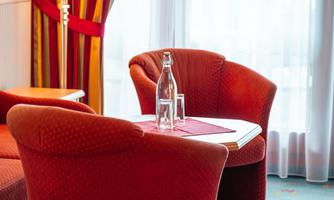 A cozy table with two red armchairs and a water carafe. The light shines through the curtains, creating an inviting atmosphere.
