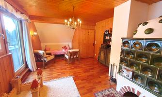 A cozy living space with wooden walls and a large window. In the room, there is a table with chairs, a stove, and a toy castle.
