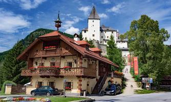 A charming, traditional house with a balcony and flowers. In the background, a historic castle rises on a hill under a blue sky.