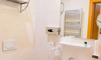 A bright bathroom with a white toilet and a sink. Towels hang on the wall and toiletries are placed on shelves.