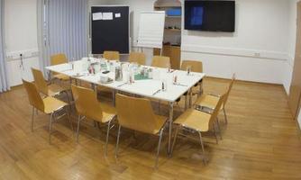 A modern meeting room with a large table and chairs. There is a television on the wall and various writing materials on the table.