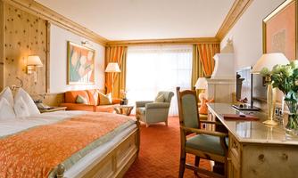 A comfortable hotel room with wooden decor and warm colors. There is a large bed, a cozy seating area, and plenty of daylight.