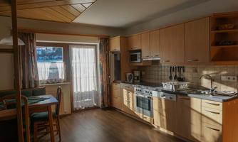A modern kitchen with wooden cabinets and a dining table. The light gently falls through the windows, creating an inviting atmosphere.