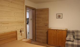 A cozy room with wood paneling, a bed, and a wooden dresser. The open door leads to another spatial unit.